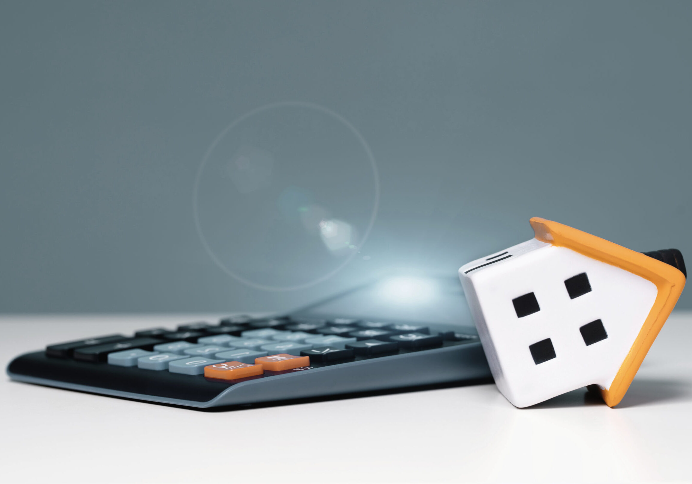 Mortgage Calculator Or Real Estate Business Concept. Office Desk mortgage calculator or real estate business concept. Office desk with a bend over house and calculator and copy space banner. Loan or insurance rate payments guidance and support. Liability and risk